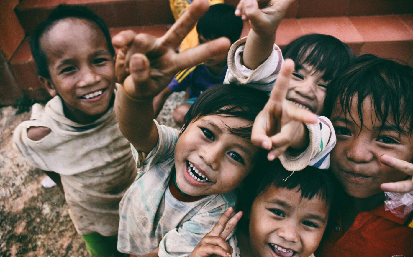 five children smiling while doing peace hand sign by Larm Rmah courtesy of Unsplash.