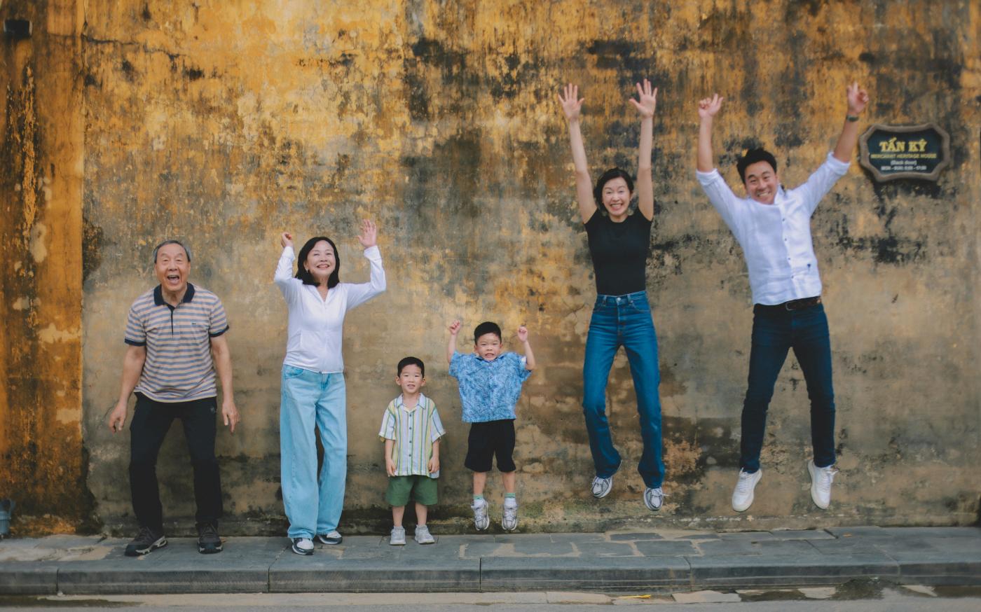 A multi-generational family jumping joyfully against a textured wall. by Hoi An and Da Nang Photographer courtesy of Unsplash.