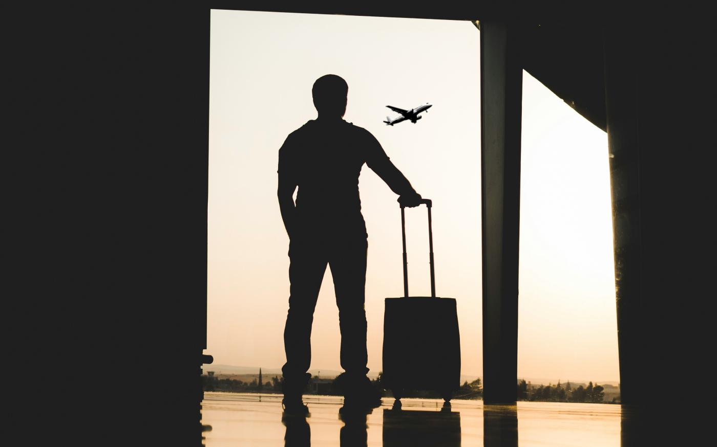 silhouette of man holding luggage inside airport by yousef alfuhigi courtesy of Unsplash.