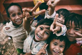 five children smiling while doing peace hand sign by Larm Rmah courtesy of Unsplash.