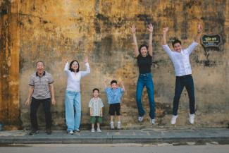 A multi-generational family jumping joyfully against a textured wall. by Hoi An and Da Nang Photographer courtesy of Unsplash.