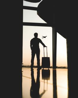 silhouette of man holding luggage inside airport by yousef alfuhigi courtesy of Unsplash.