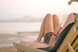 a woman laying on a beach chair reading a book by Kostiantyn Li courtesy of Unsplash.