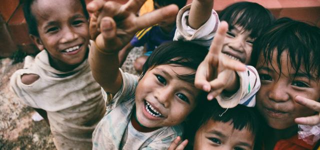 five children smiling while doing peace hand sign by Larm Rmah courtesy of Unsplash.