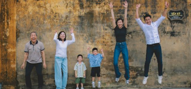 A multi-generational family jumping joyfully against a textured wall. by Hoi An and Da Nang Photographer courtesy of Unsplash.